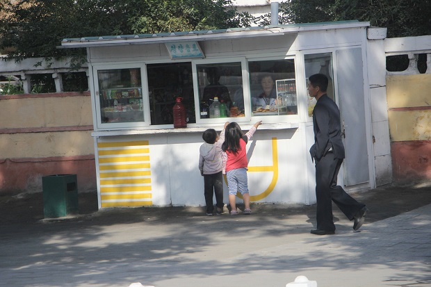 Kids buying snacks at a local roadside shop as a man in suit dress pass by. 